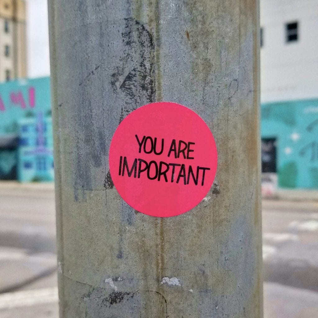 You are important, supportive message on a pink sticker on a city pole in an urban setting.